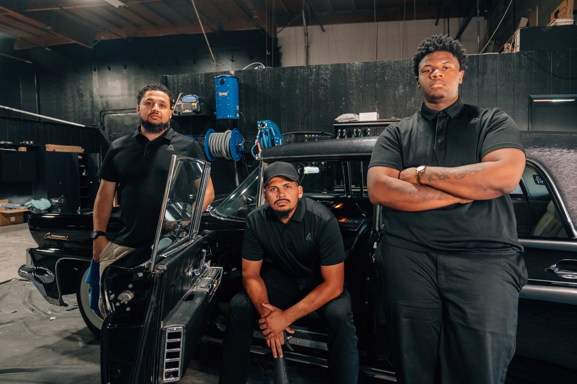 Moody's Extreme Detailing crew standing around a classic black Lincoln Continental inside the shop